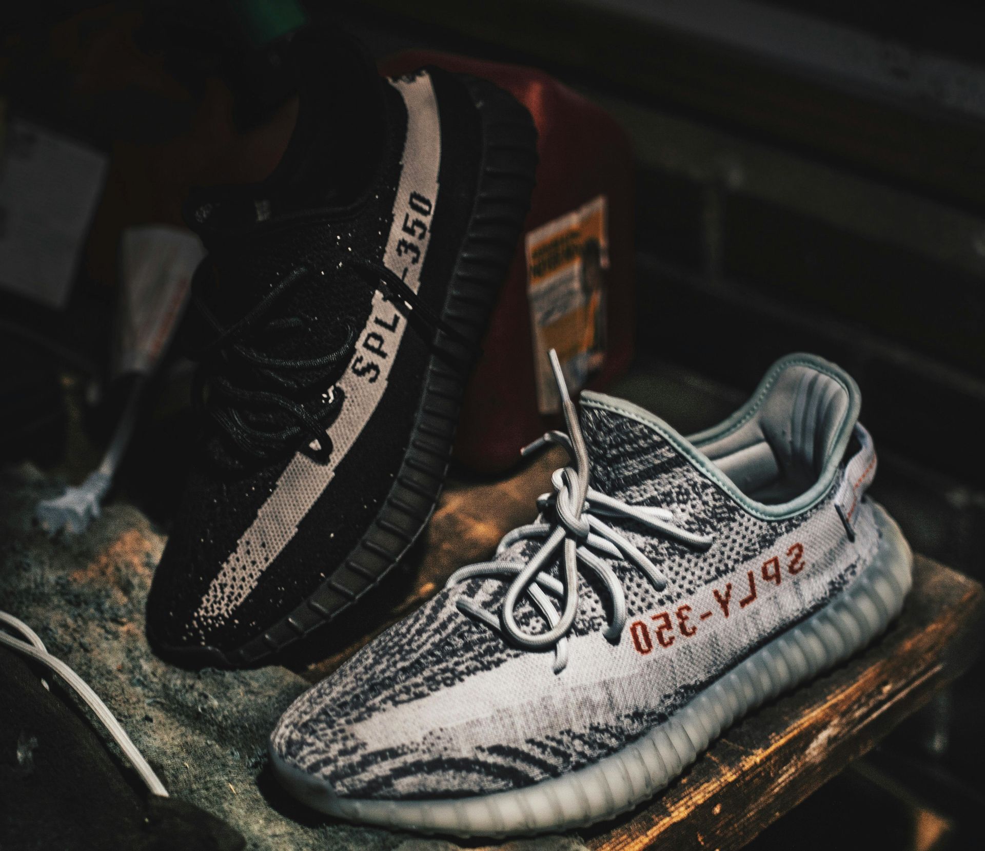 两双 Adidas Yeezy 350 运动鞋：黑色和白色，放在质朴的木质表面上。