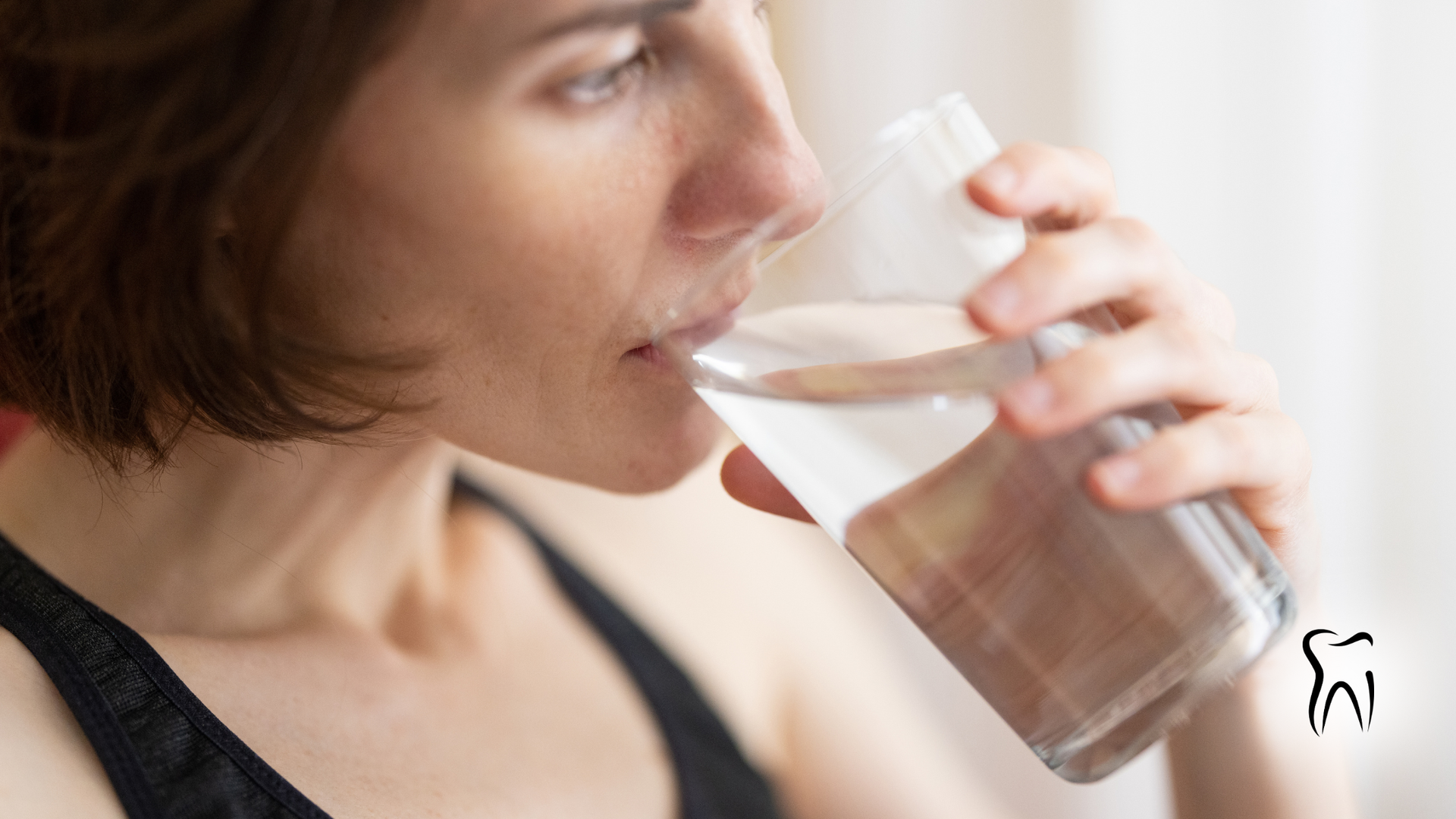 Woman drinking water from a clear glass, indoors.