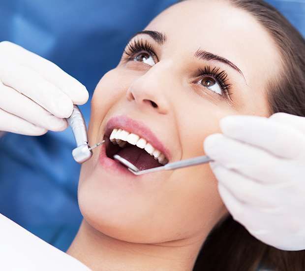 Woman at dentist, mouth open, being examined with tools. Wearing blue, smiling.