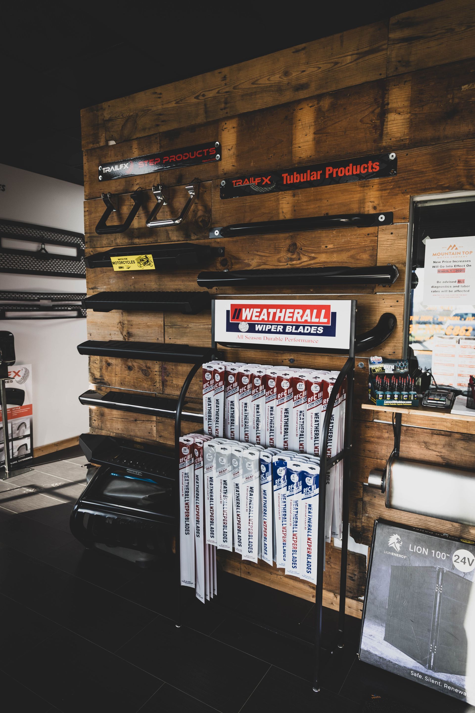 Display of automotive parts and products in a shop, including racks, shelves, and signs against a wooden background. | Mountain Top Service Center