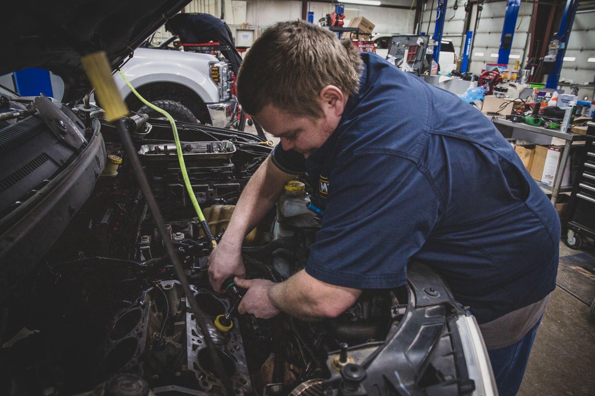 Mechanic working on car engine in a repair shop, wearing blue shirt, using tools. | Mountain Top Service Center