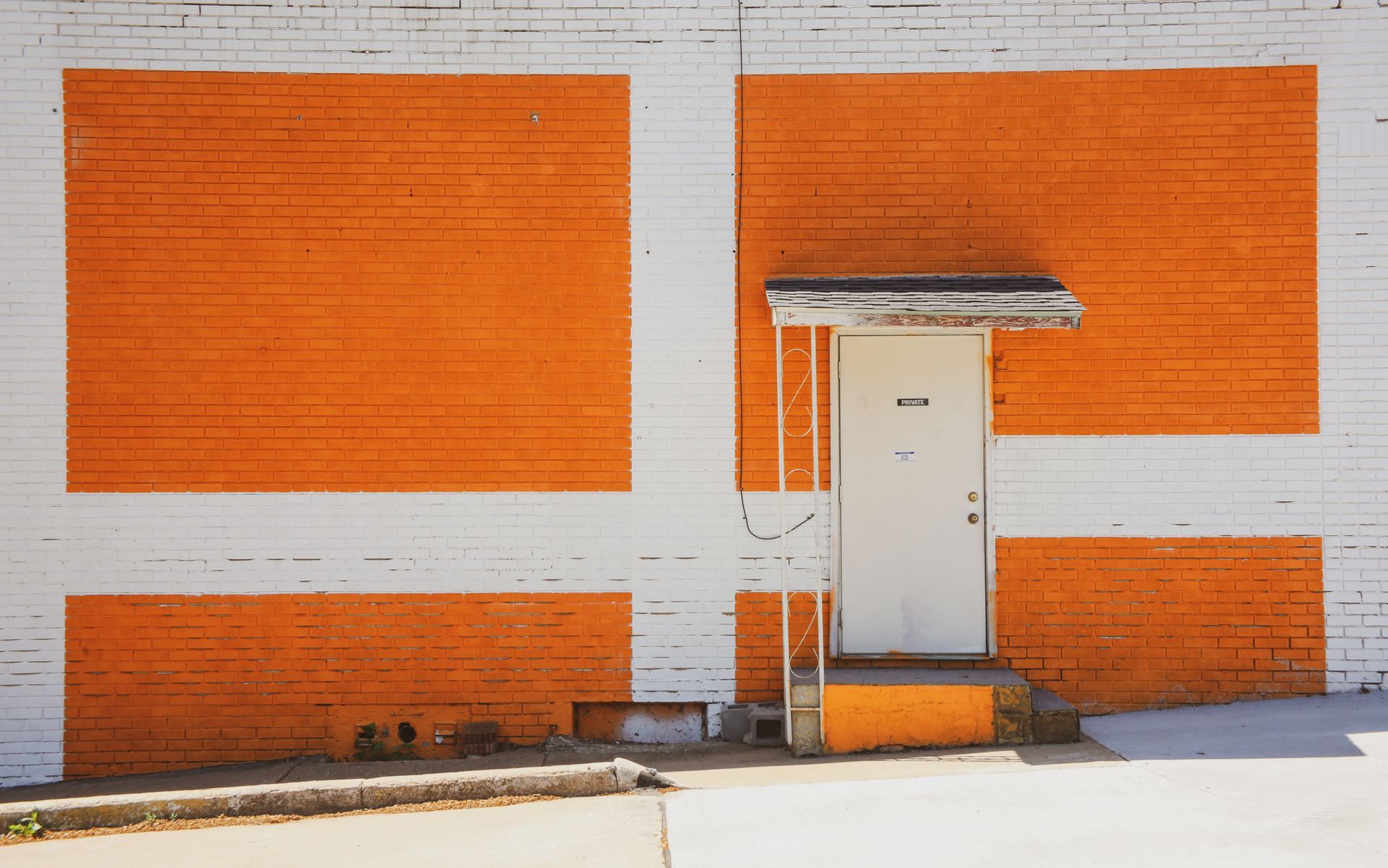 White brick building with orange geometric design and a white door under a small awning.