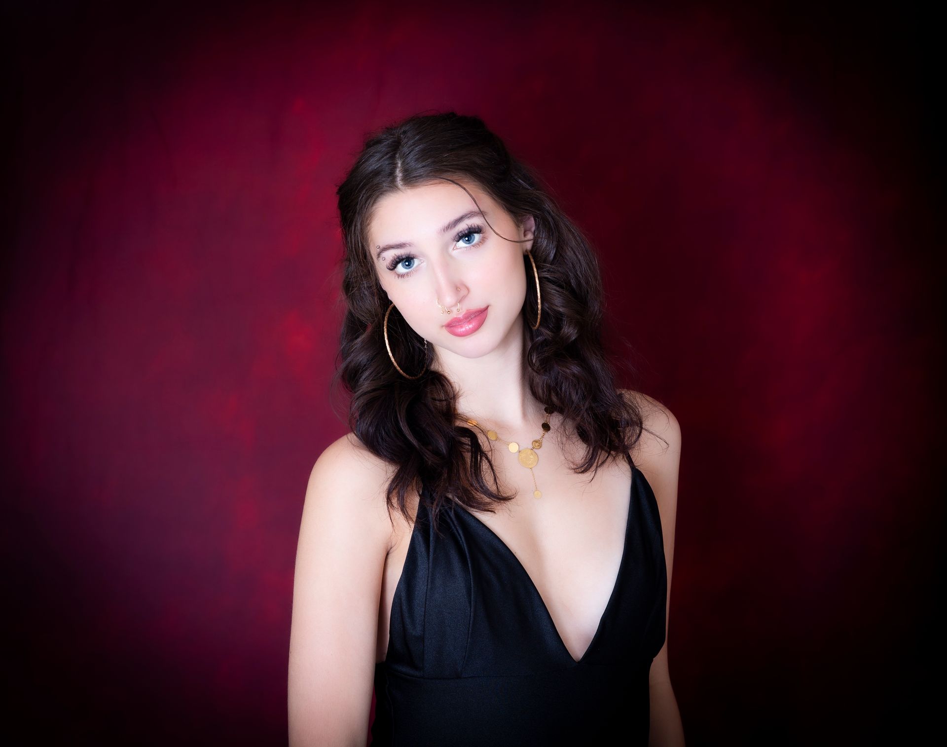 Woman with dark hair and a black dress poses against a burgundy background.