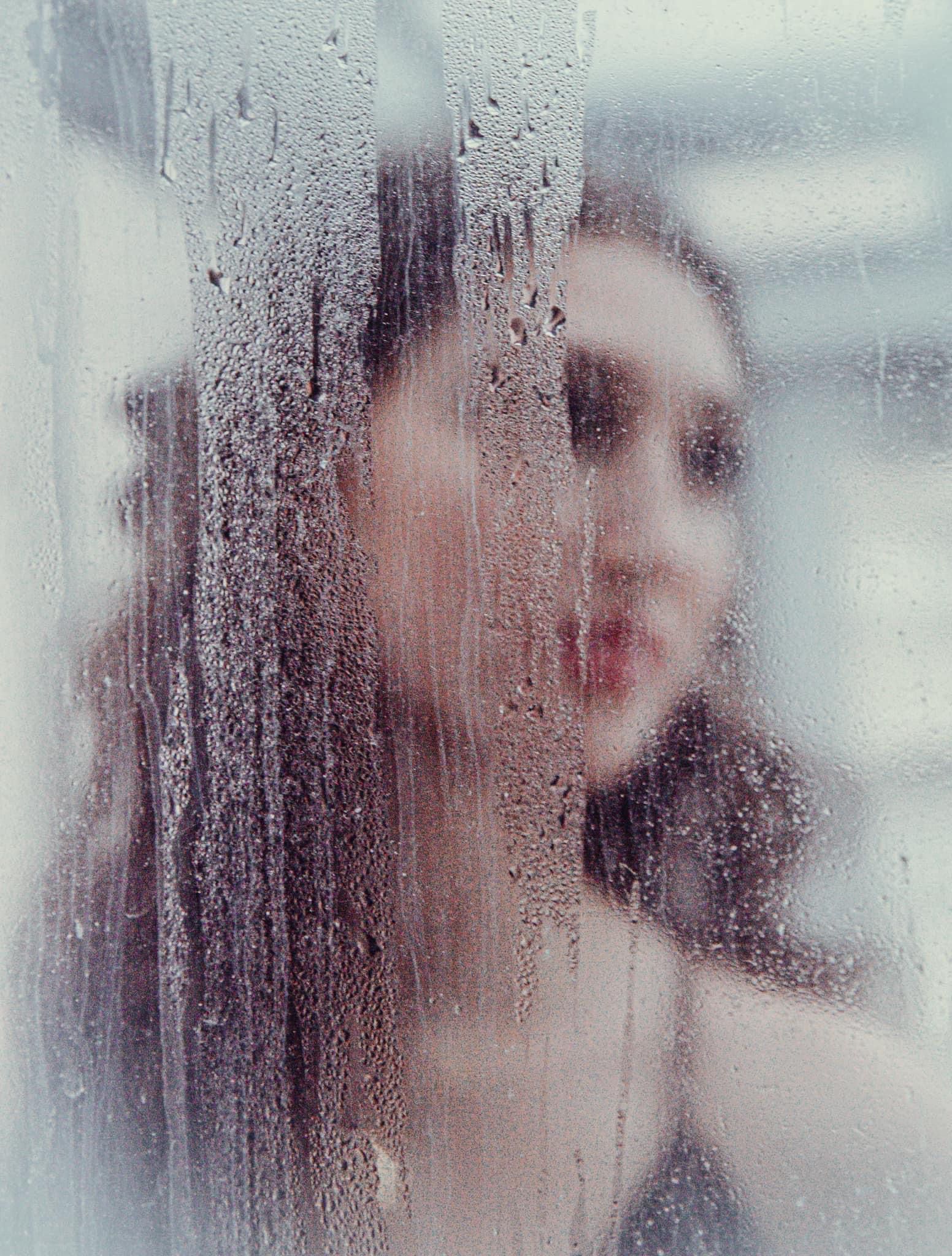 Woman's face blurred behind steamy glass, red lips visible. Dark hair, black top.