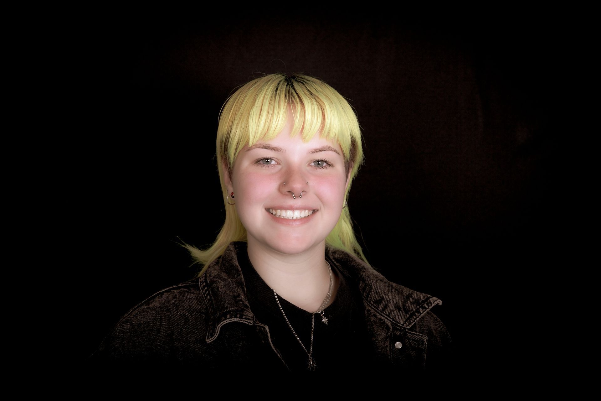 Young person with yellow hair smiles against a black background.