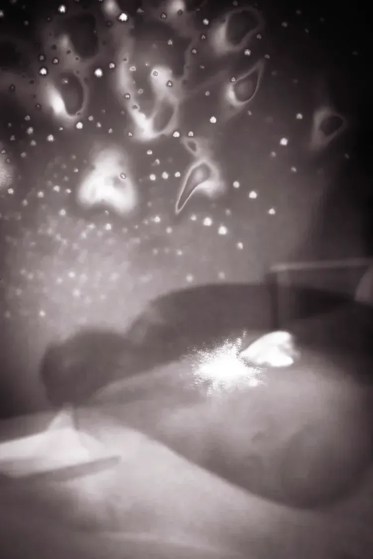 Dreamlike black and white: glowing form with bright spot, surrounded by light and stars.