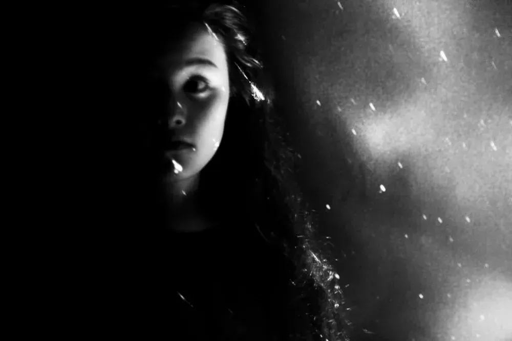 A young girl in the dark looks up, illuminated by a light with falling snow or sparks.