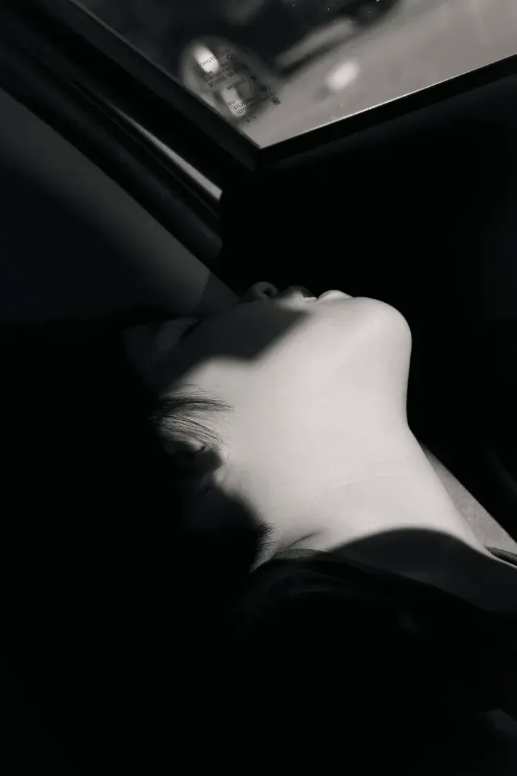 Black and white portrait. Person's face tilted up, lit by sunlight from a window; in shadow.