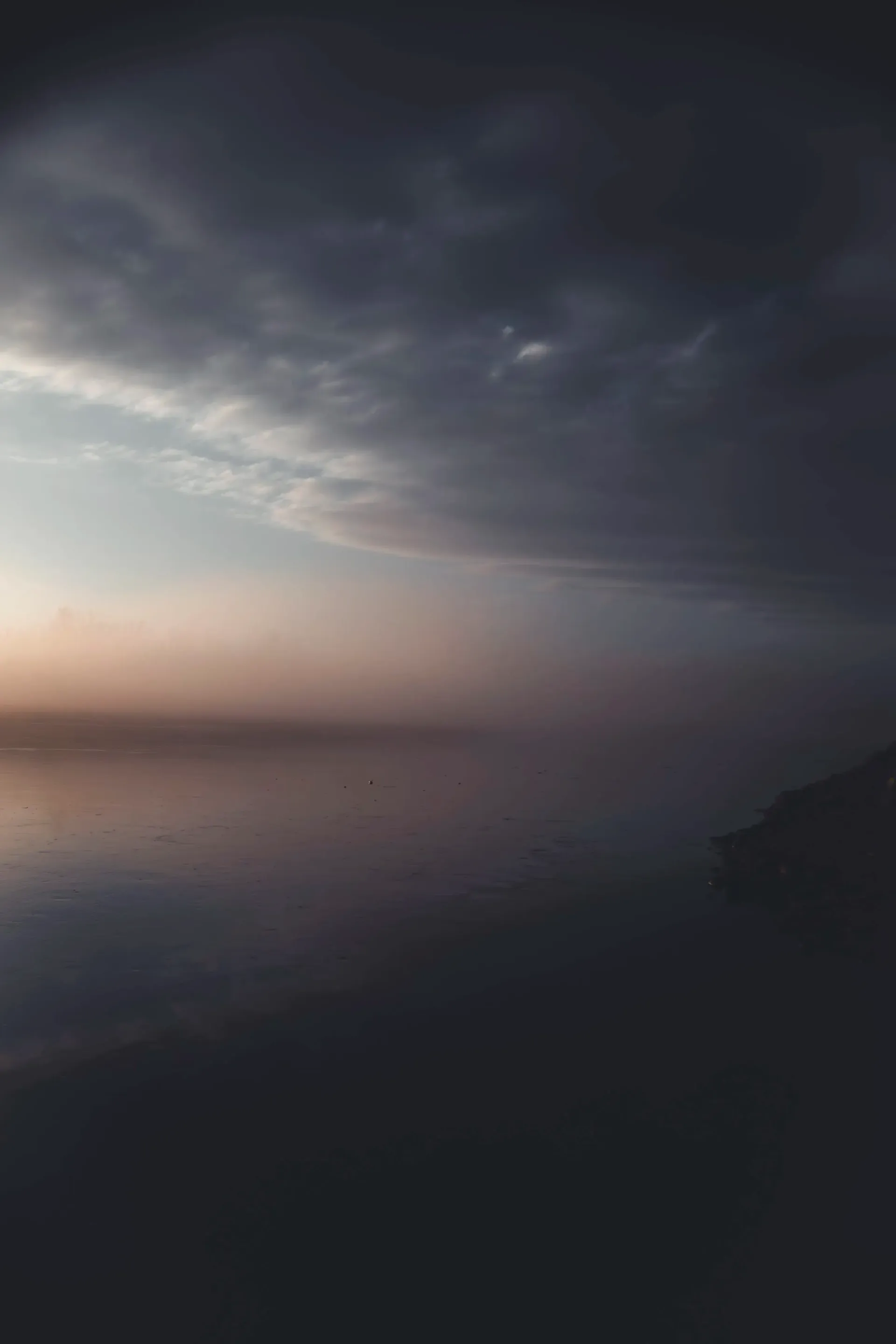 Gloomy coastal scene: dark water reflects a cloudy sky with hints of pink and purple.