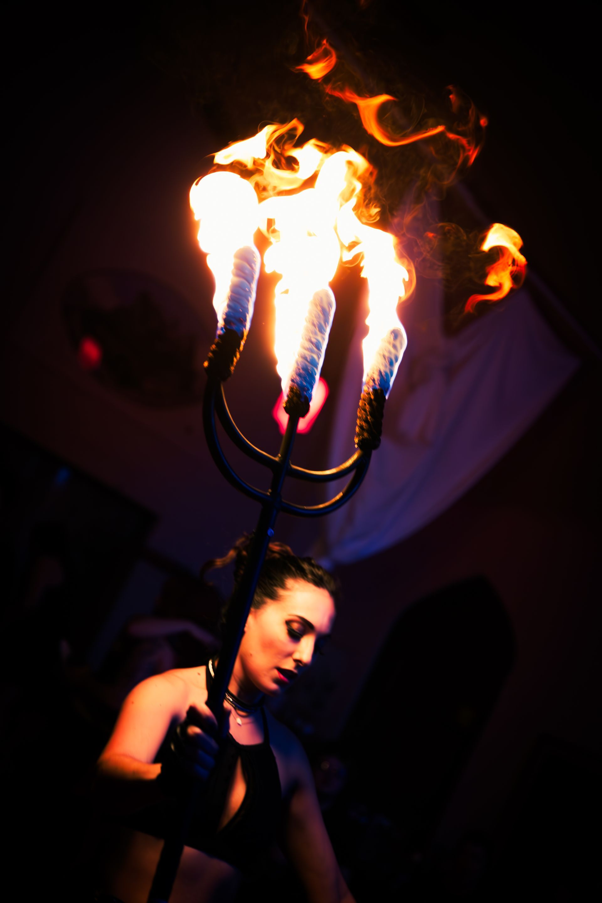 Woman holds a flaming trident aloft in a dimly lit setting.