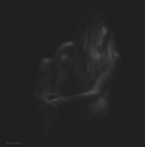 Black and white, blurred image of a woman embracing herself; long hair, low light.