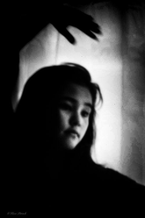 Woman's face in soft focus, shadowed with a hand above, black and white.