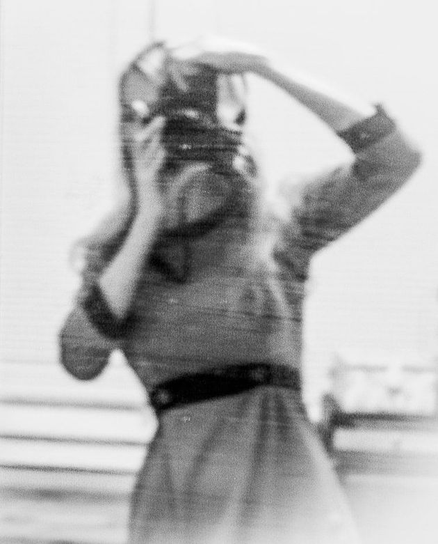 Woman in dress holding a camera, taking a photo. Black and white, blurry.
