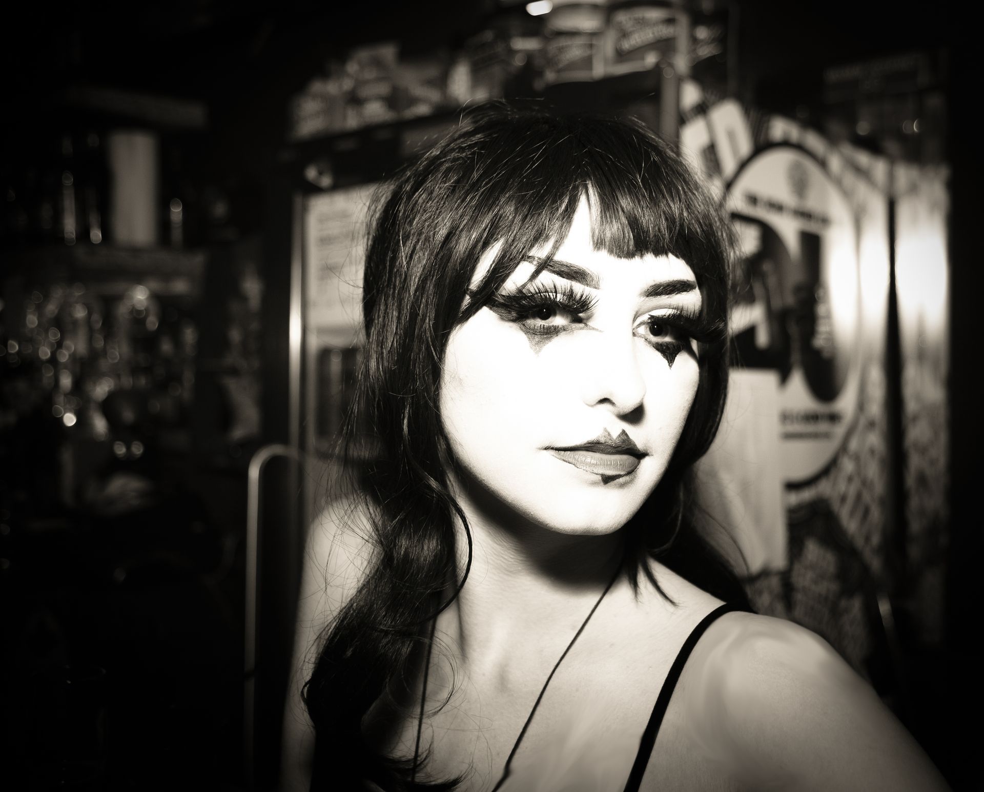 Woman with dark makeup, hair, and a low-cut black top in a dimly lit bar setting.