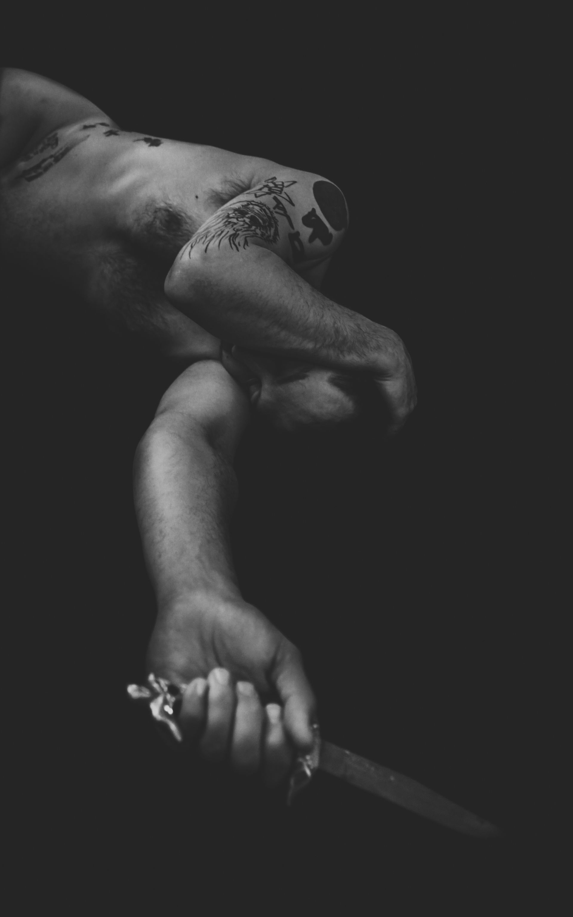 A black and white image of a person holding a knife, with a partially visible body and a dark setting.
