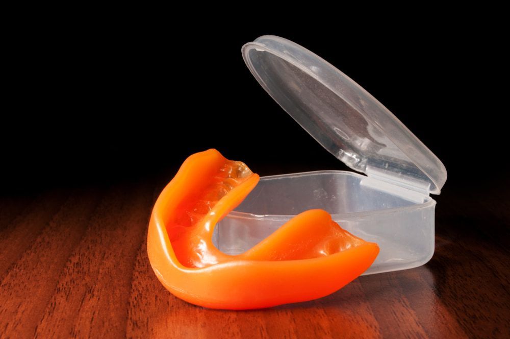 An Orange Mouth with A Plastic Case on A Wooden Table — Bromley's Denture Clinic in Tweed Heads South, NSW