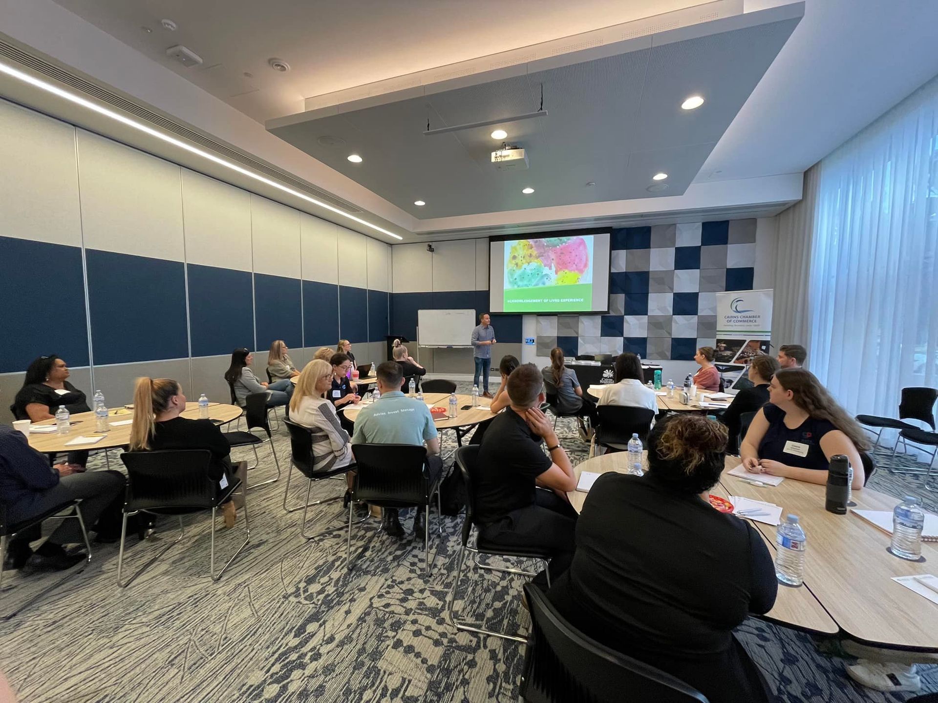 People in a meeting room, listening to a presentation on a screen.