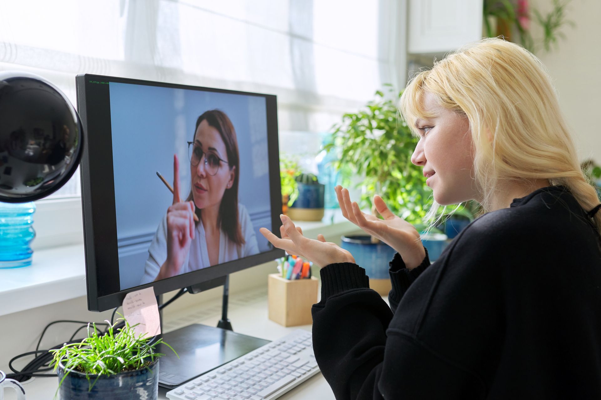 Woman on video call gestures, looking at a monitor displaying another woman pointing a finger, in a home office setting. Woman on video call gestures, looking at a monitor displaying another woman pointing a finger, in a home office setting.