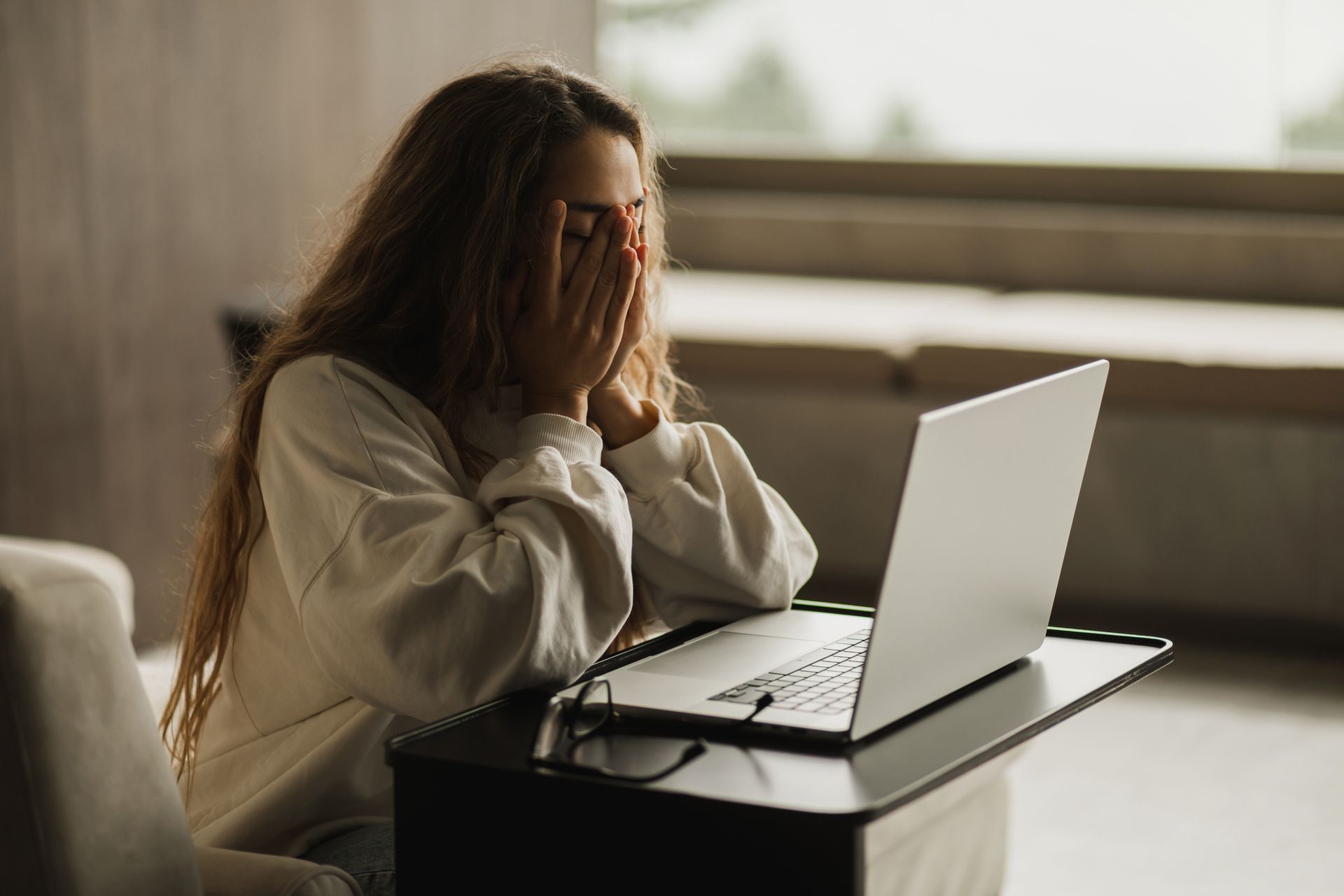 Person sitting at a laptop, covering their face with hands, looking stressed. Person sitting at a laptop, covering their face with hands, looking stressed.