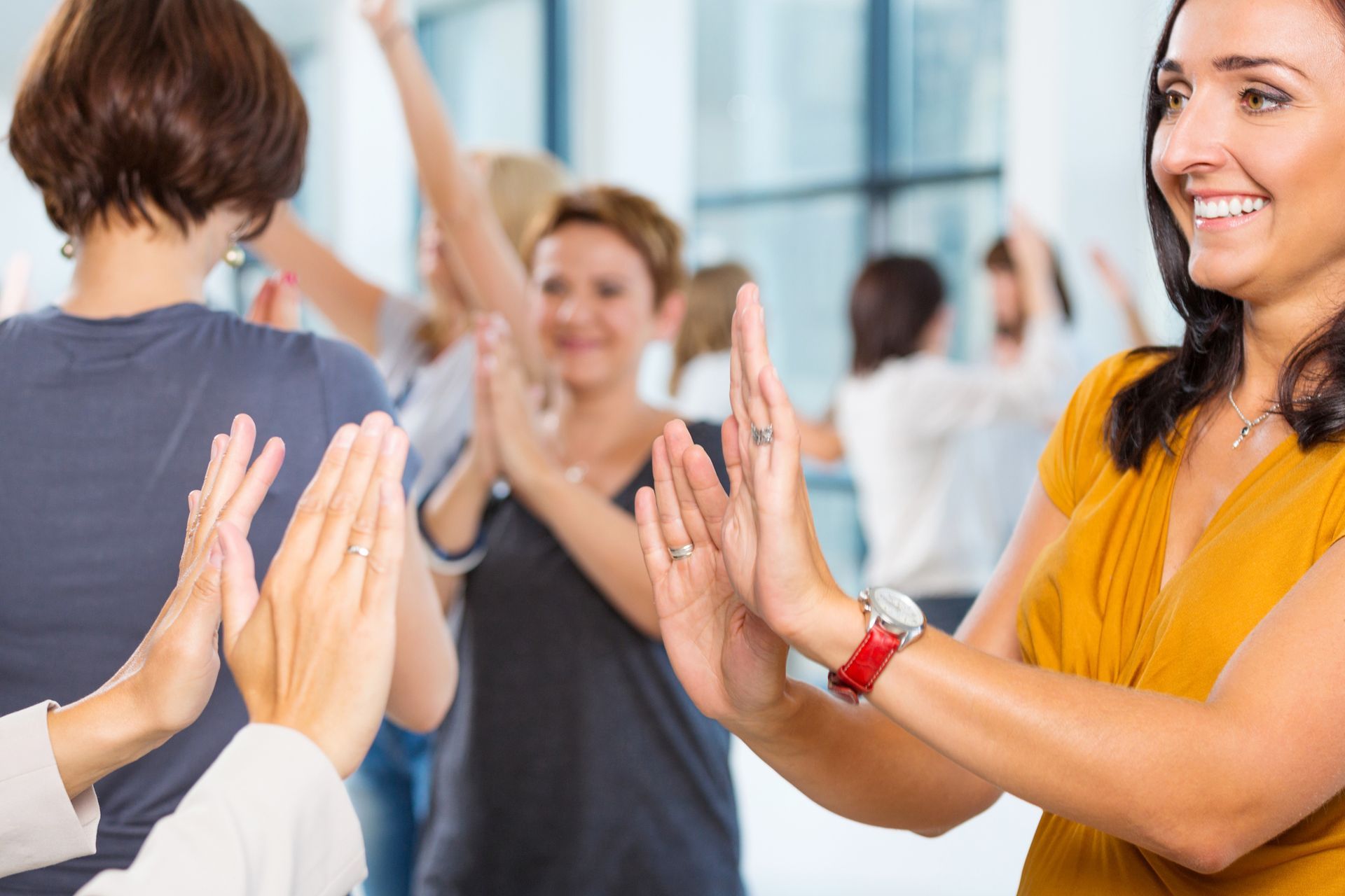 People clapping in a bright office setting. Woman in yellow top smiles, others in background.