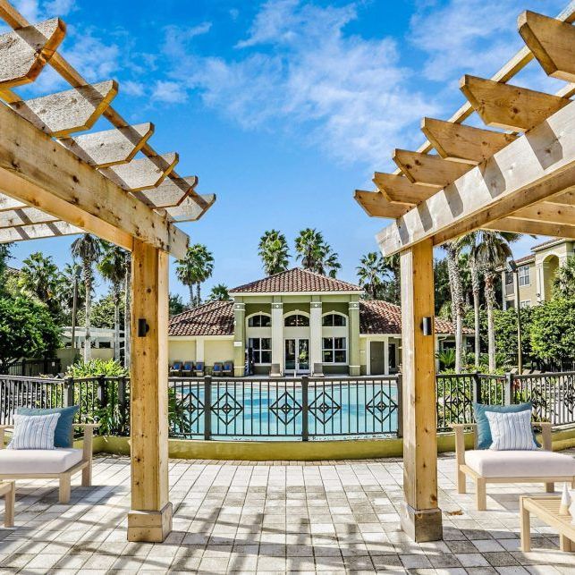 A pergola overlooking a swimming pool with a house in the background