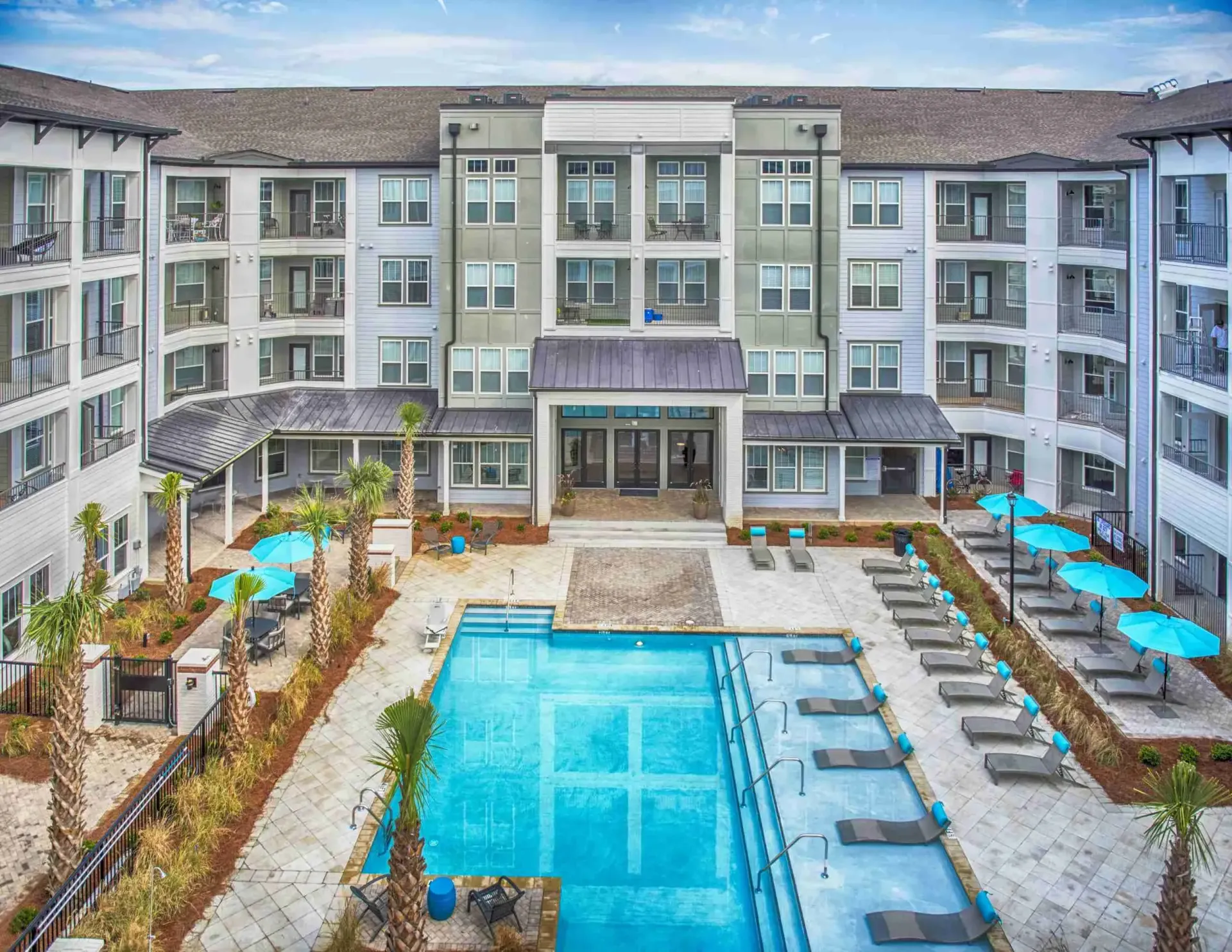 Apartment complex with pool, lounge chairs, and palm trees under a blue sky.