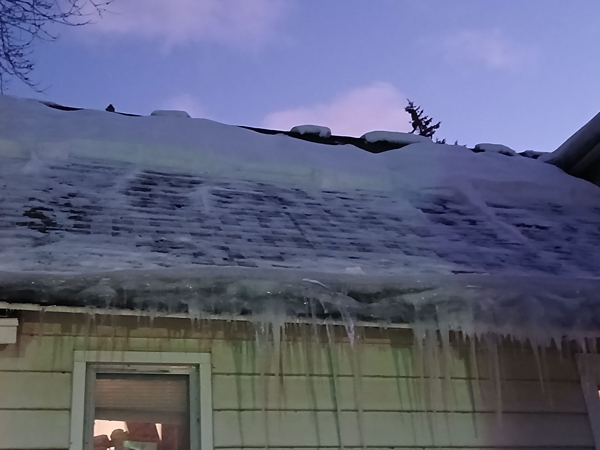 Icicle-covered roof above a house doorway at dusk with a purple sky