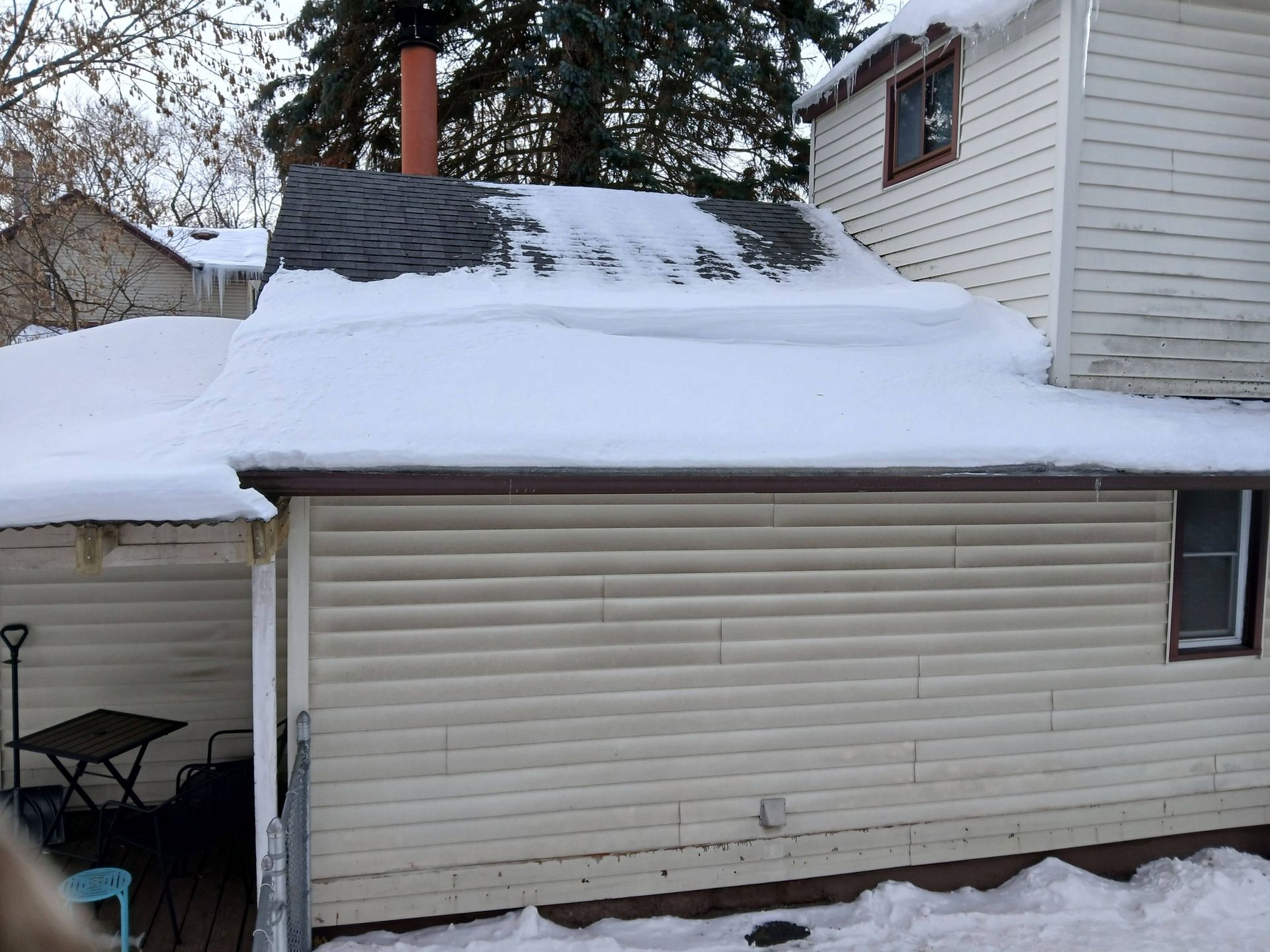 Snow-covered garage roof and beige siding beside a house in a winter yard