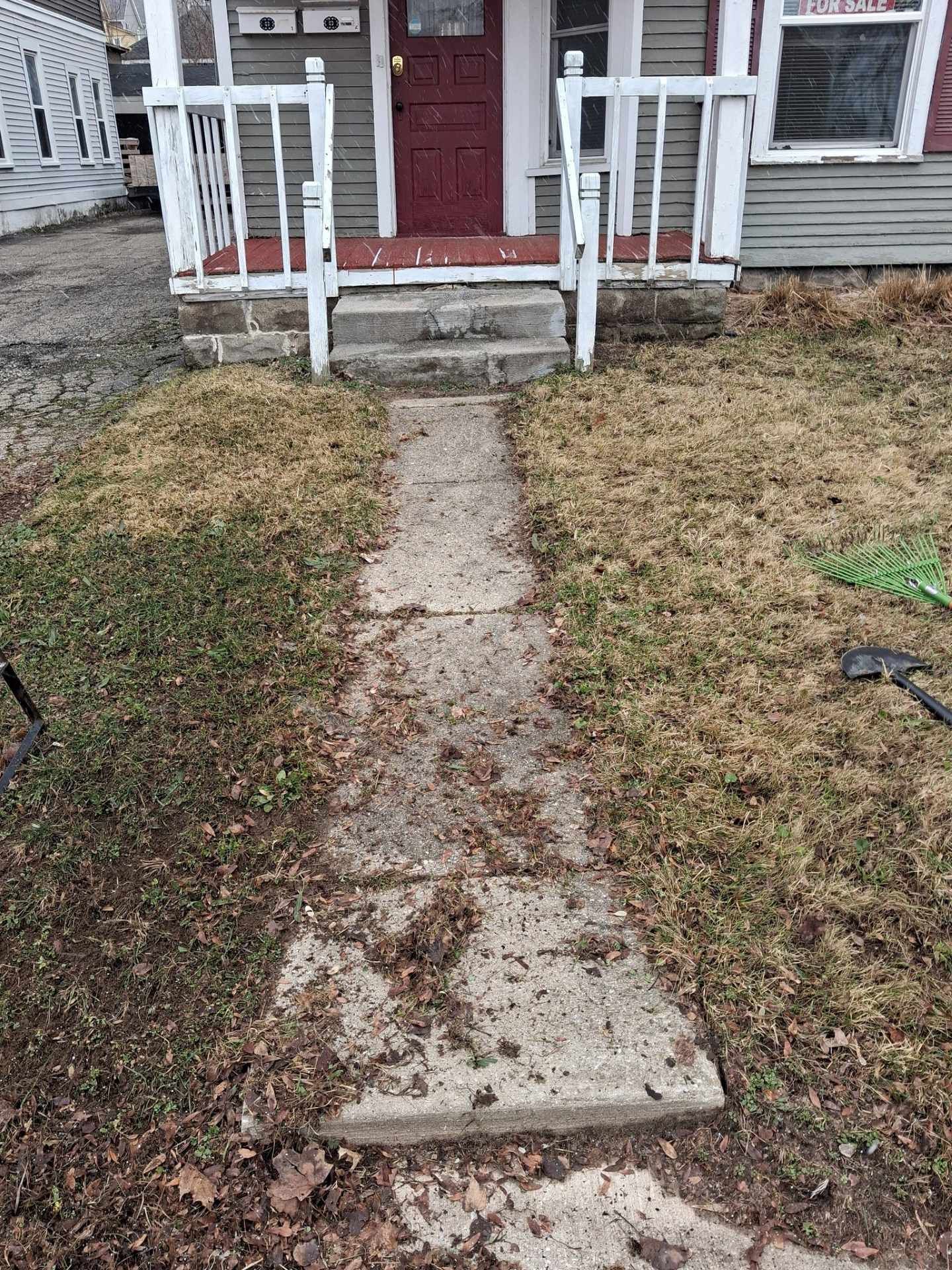 Front walkway leading to a red house porch, with cracked concrete and patchy grass on both sides