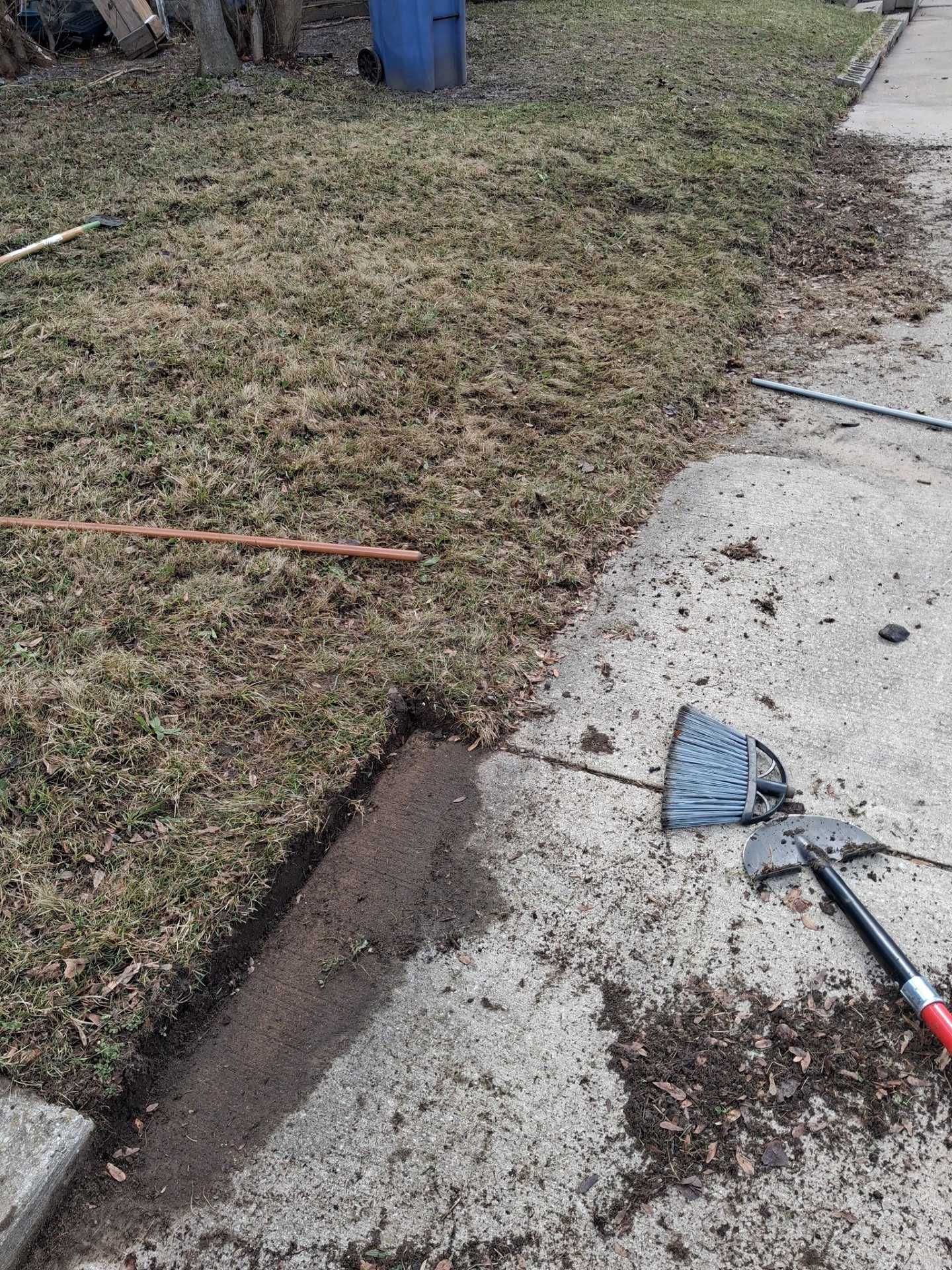 Concrete driveway edge being cleaned with a shovel beside a grassy yard.