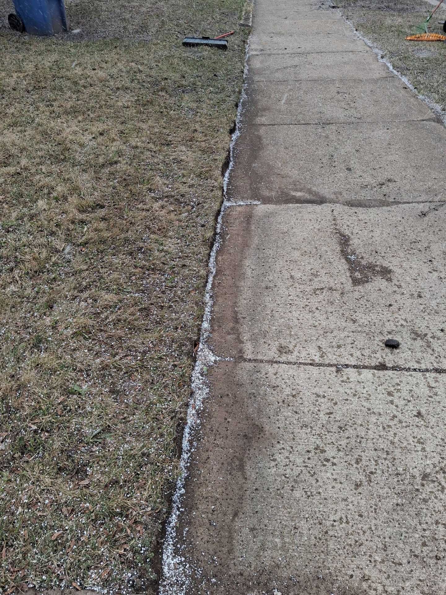 Concrete sidewalk beside a patchy brown lawn with a white painted edge line.