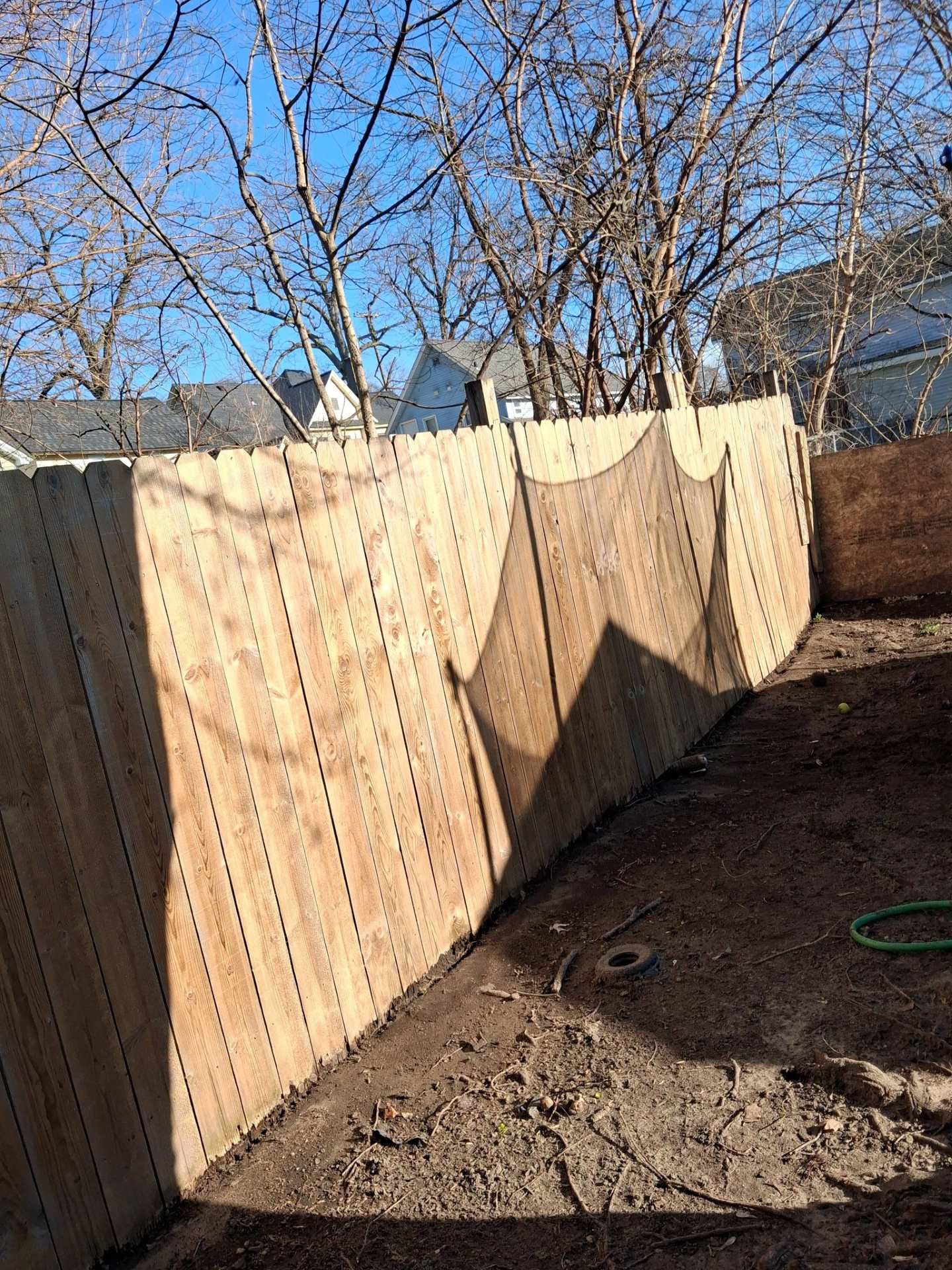 Wooden fence casting shadows in a bare backyard under a clear blue sky