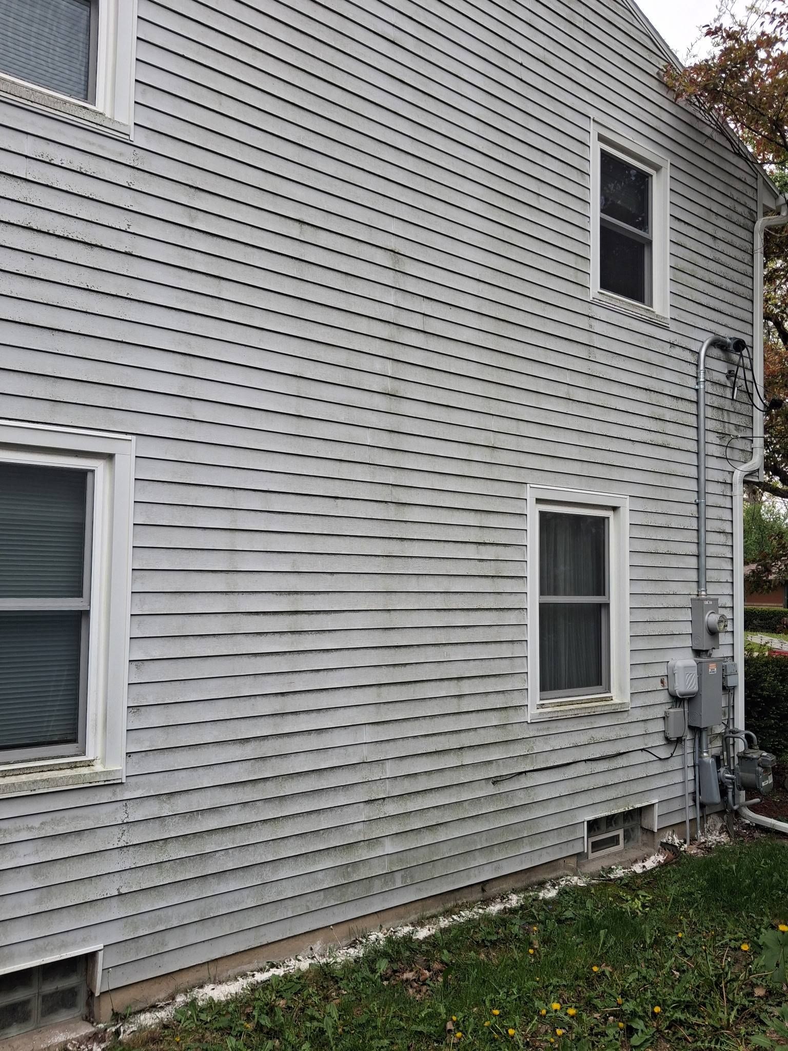 Side of a white vinyl-sided house with windows, utility meters, and a small grassy yard.