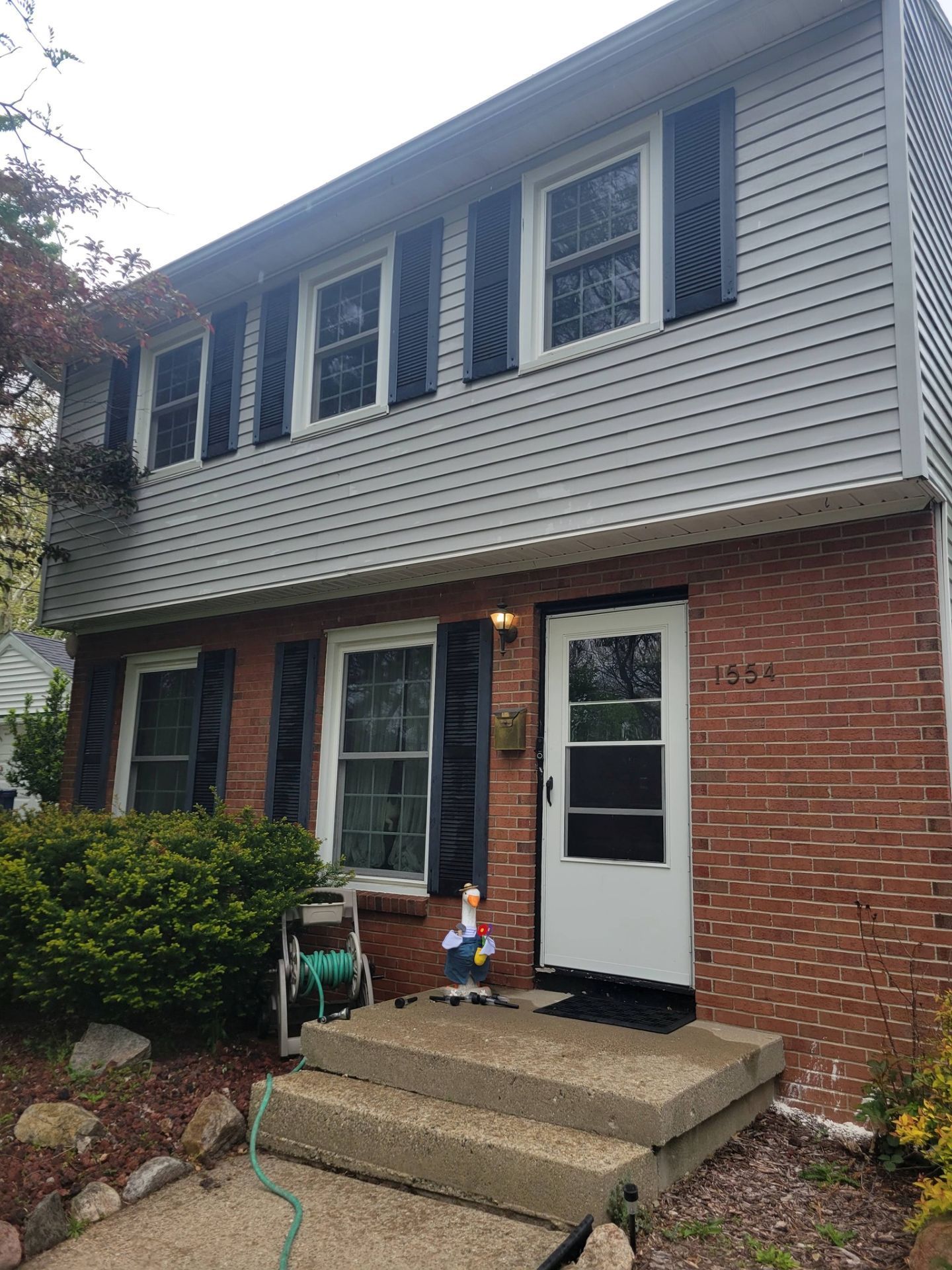 Two-story brick-and-siding townhouse with front steps, white door, and lit porch in a leafy yard
