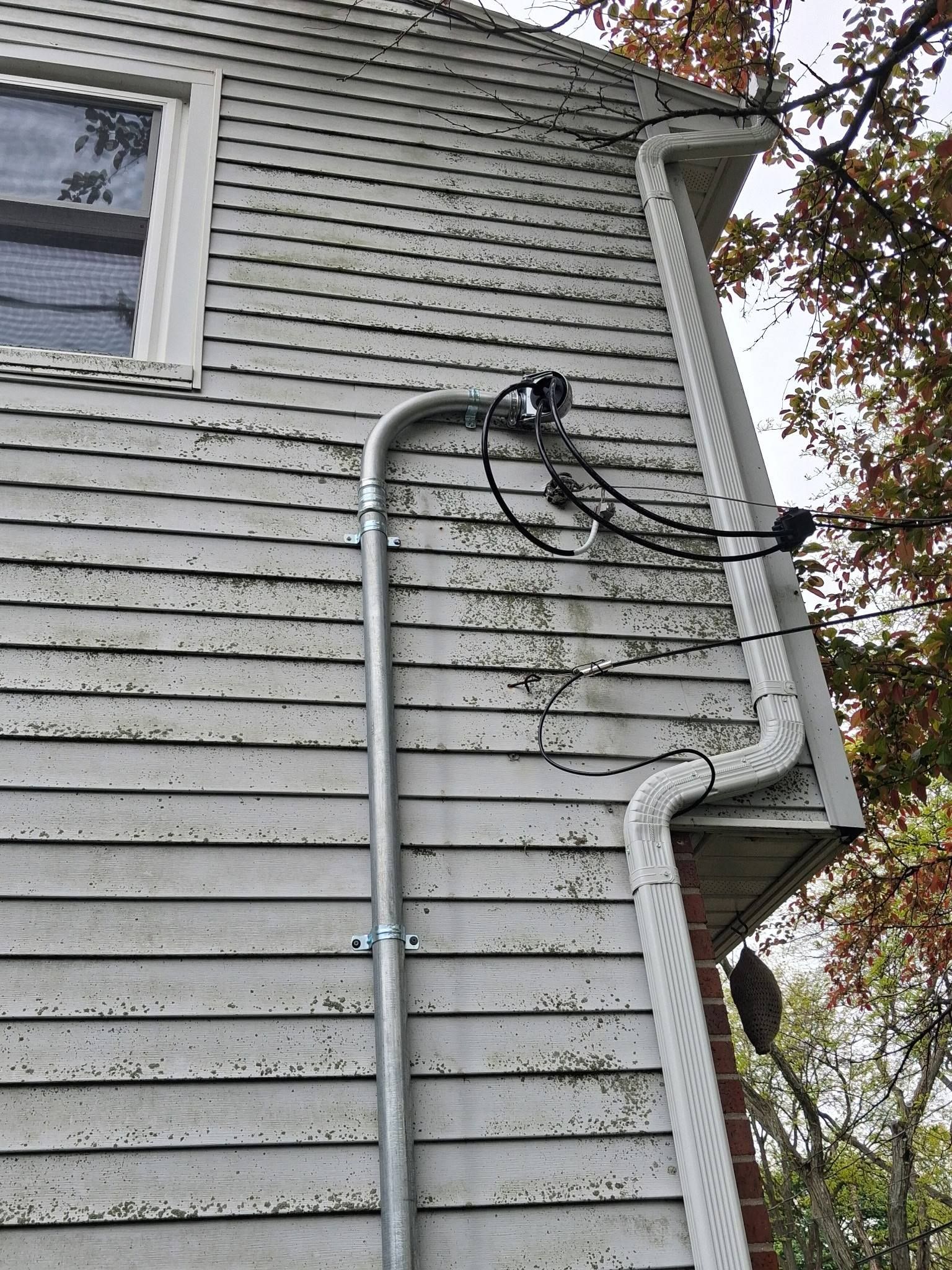 Gray house siding with exposed electrical conduit and overhead wires near a window