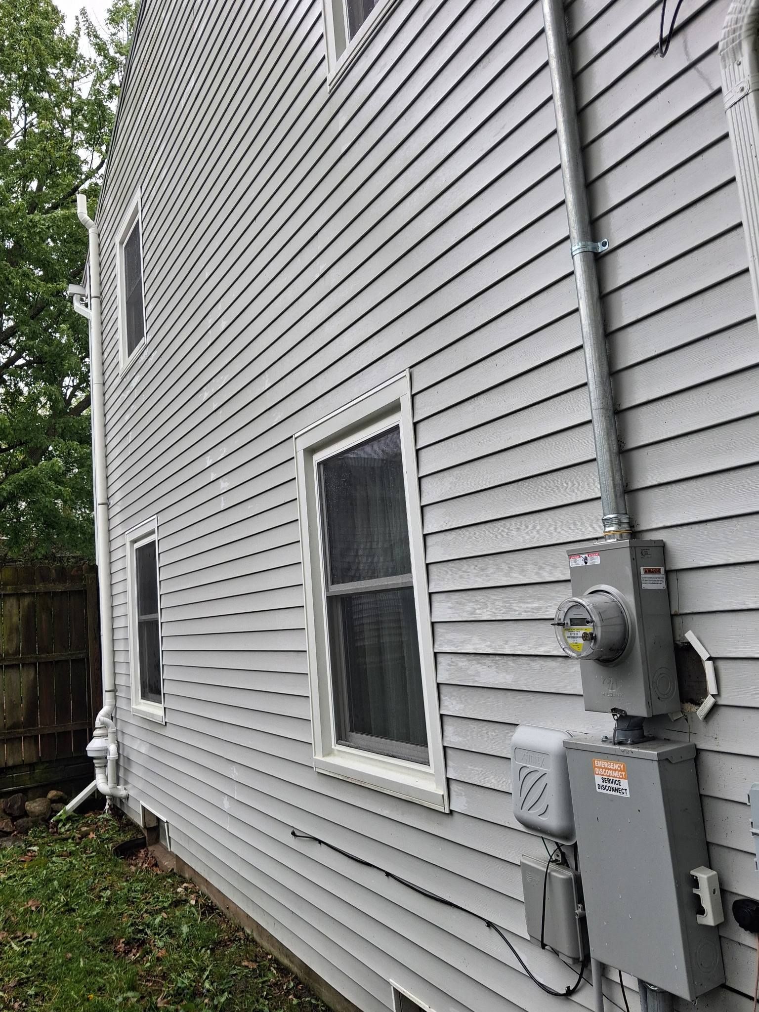 Side of a white vinyl-sided house with windows, utility meters, and grassy yard.