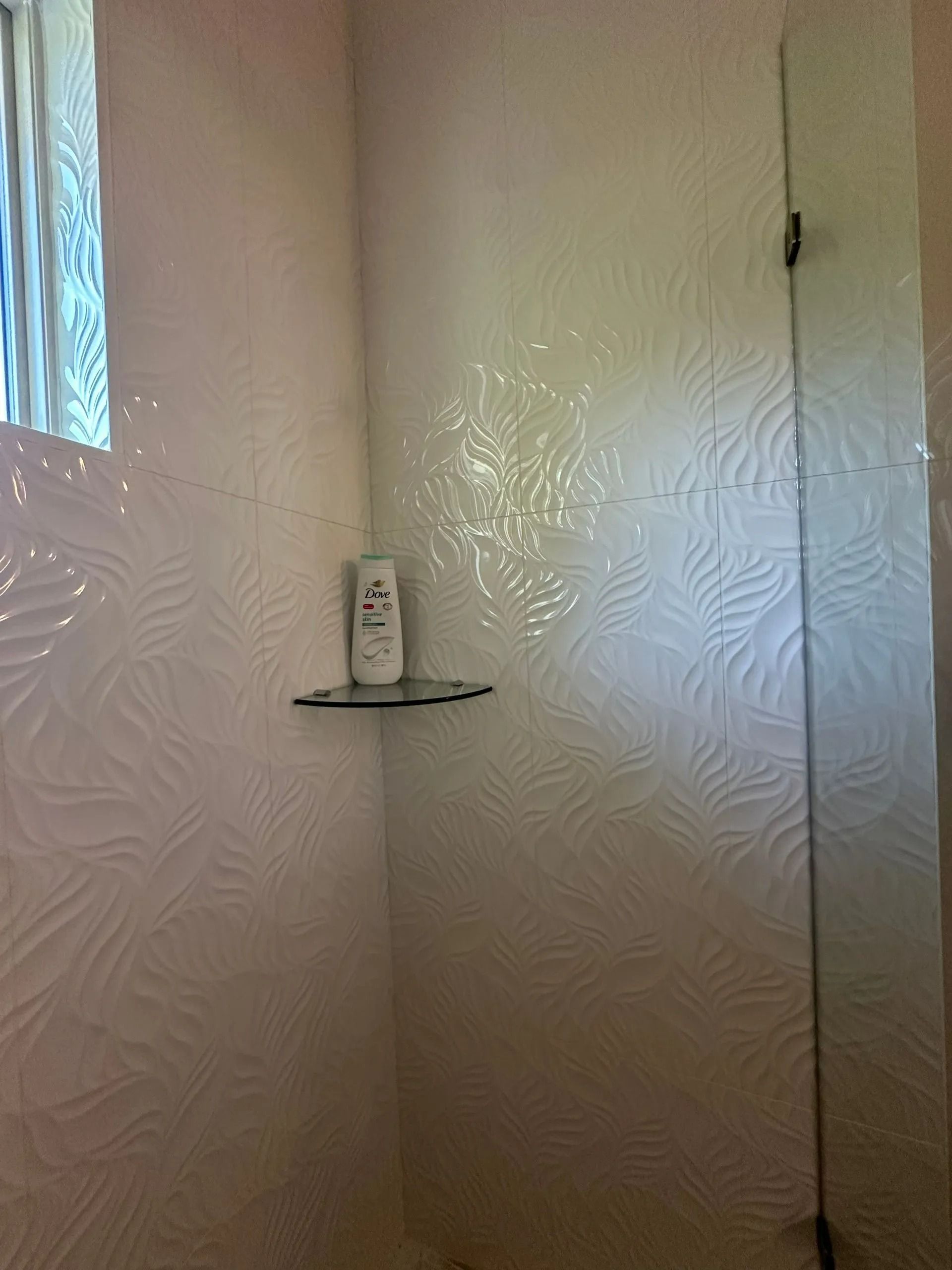 A bathroom with a shower and a shelf with a bottle of lotion on it.