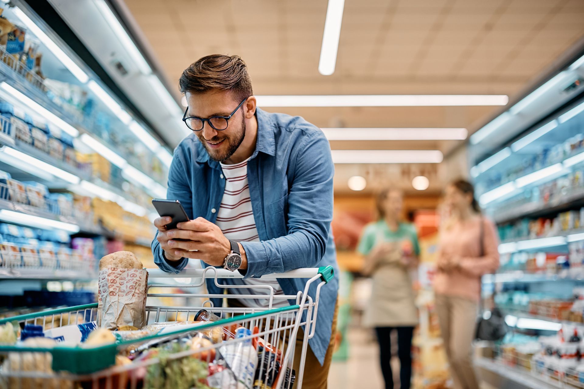 Man with shopping cart grocery shopping and looking at phone