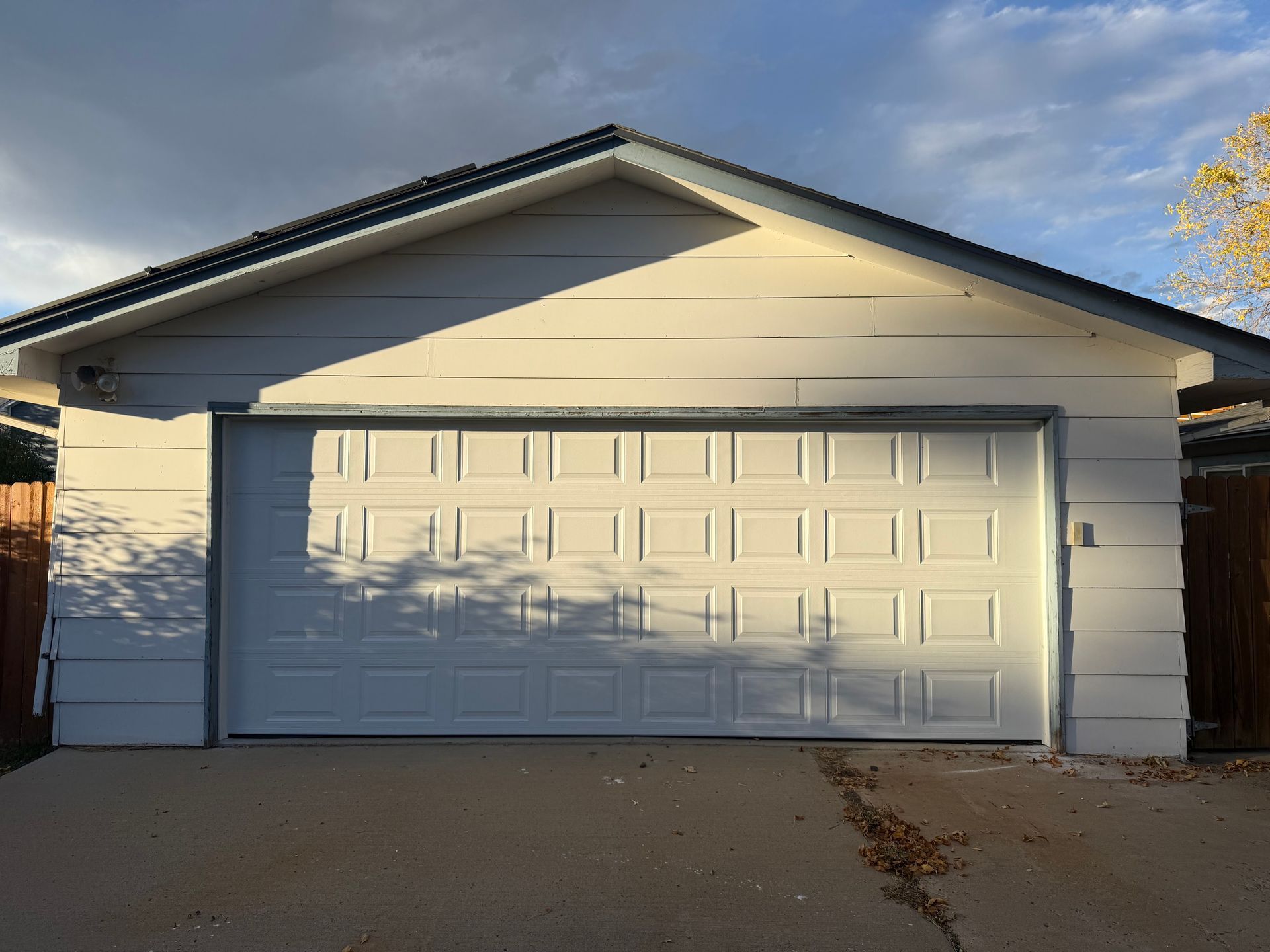 A detached, white, single-car garage with a panelled white door under a gabled roof against a blue sky.