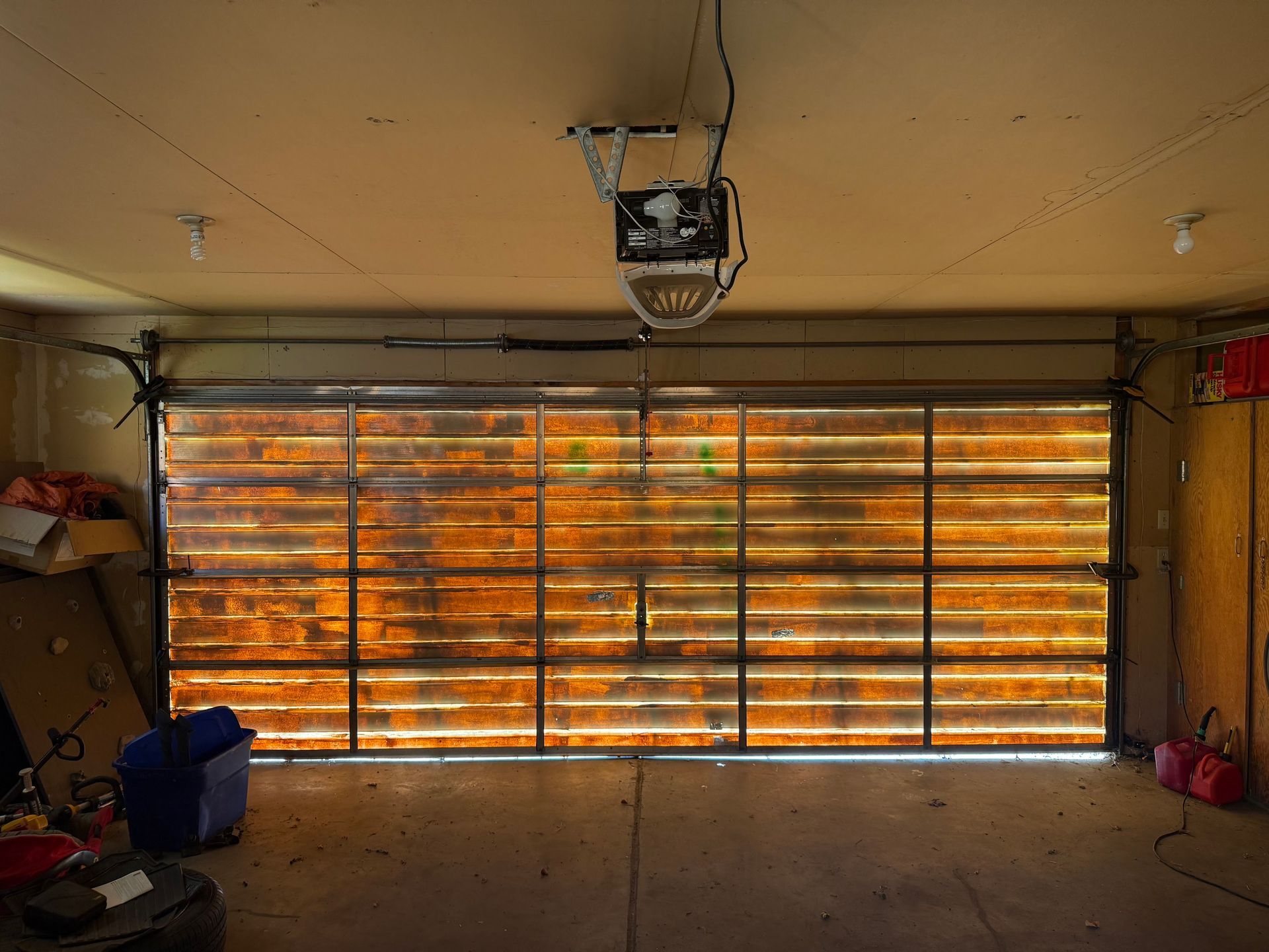 A garage door with horizontal glass panels allowing warm, bright daylight to shine through into the dim garage.