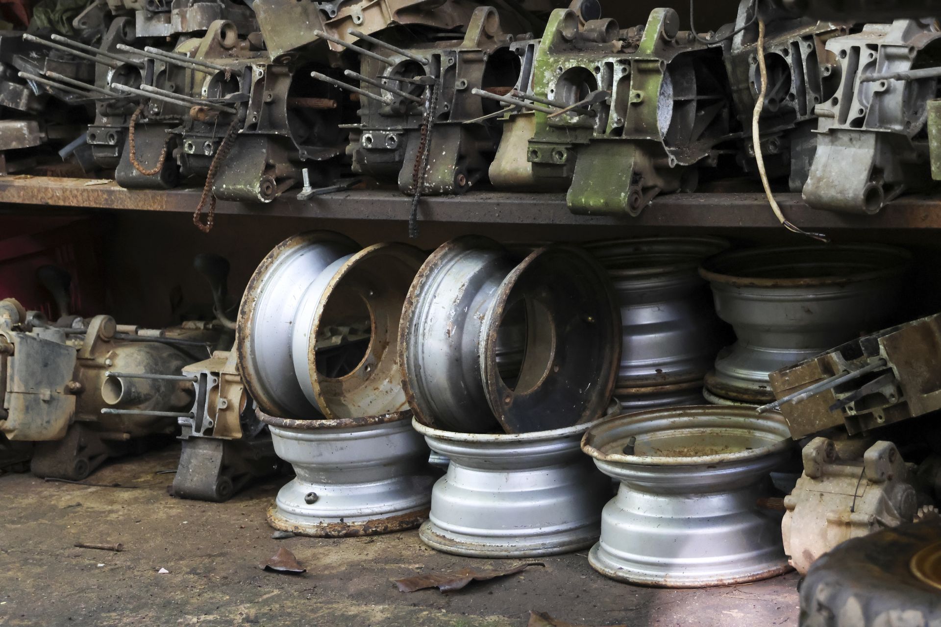 Metal wheel rims and engine components pile up in a cluttered garage. Metal wheel rims and engine components pile up in a cluttered garage.