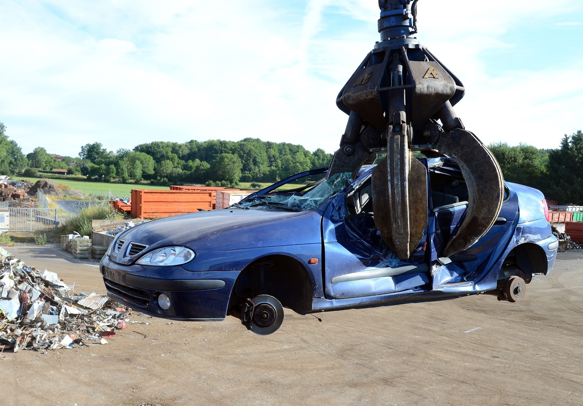 A blue car suspended in the air by a crane, showcasing the lifting process at a recycling location.