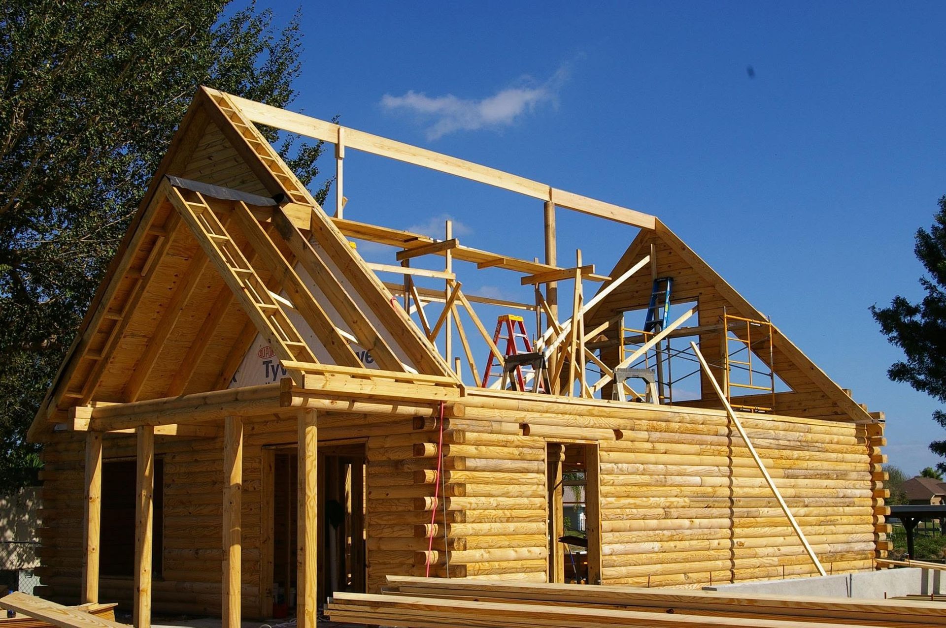 Wooden house under construction with exposed roof framing against a blue sky.