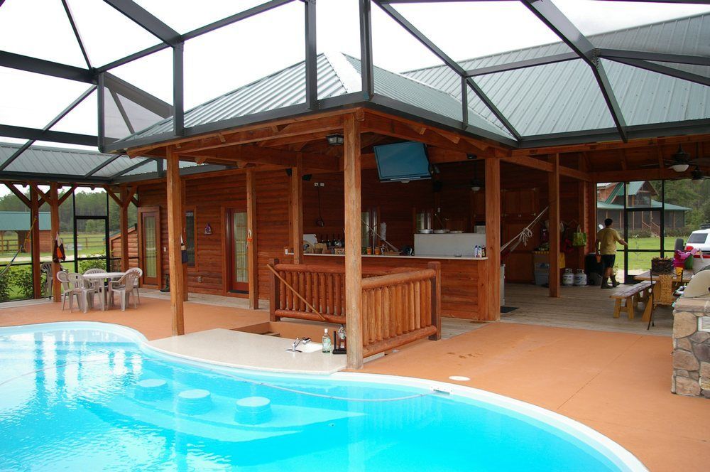 Poolside wooden cabana with bar seating beside a turquoise swimming pool under a covered patio