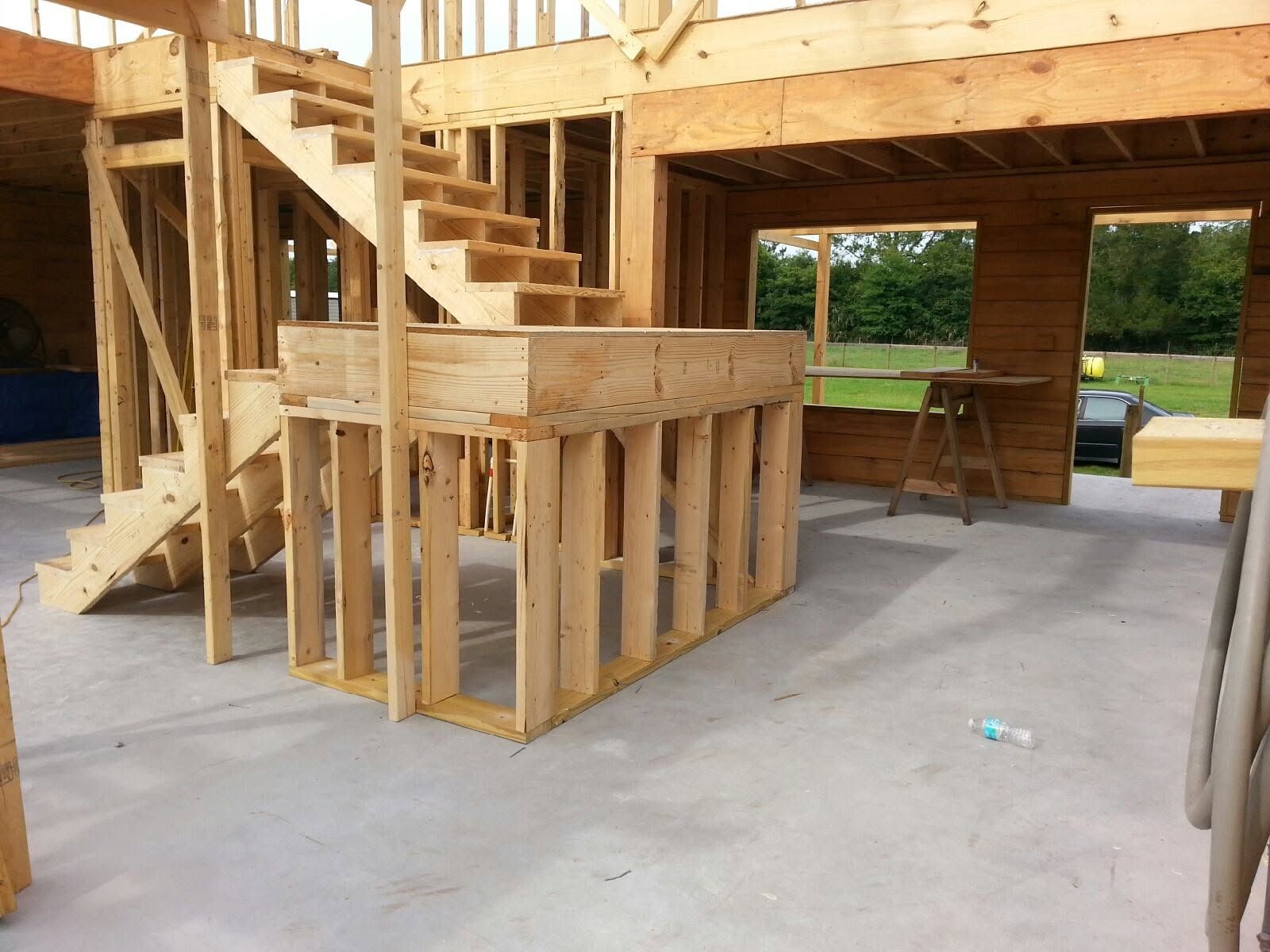 Unfinished wooden house framing with stairs and a covered porch on a concrete slab