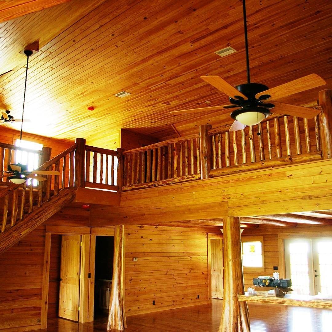 Wood-paneled cabin interior with loft balcony, ceiling fans, and warm natural light