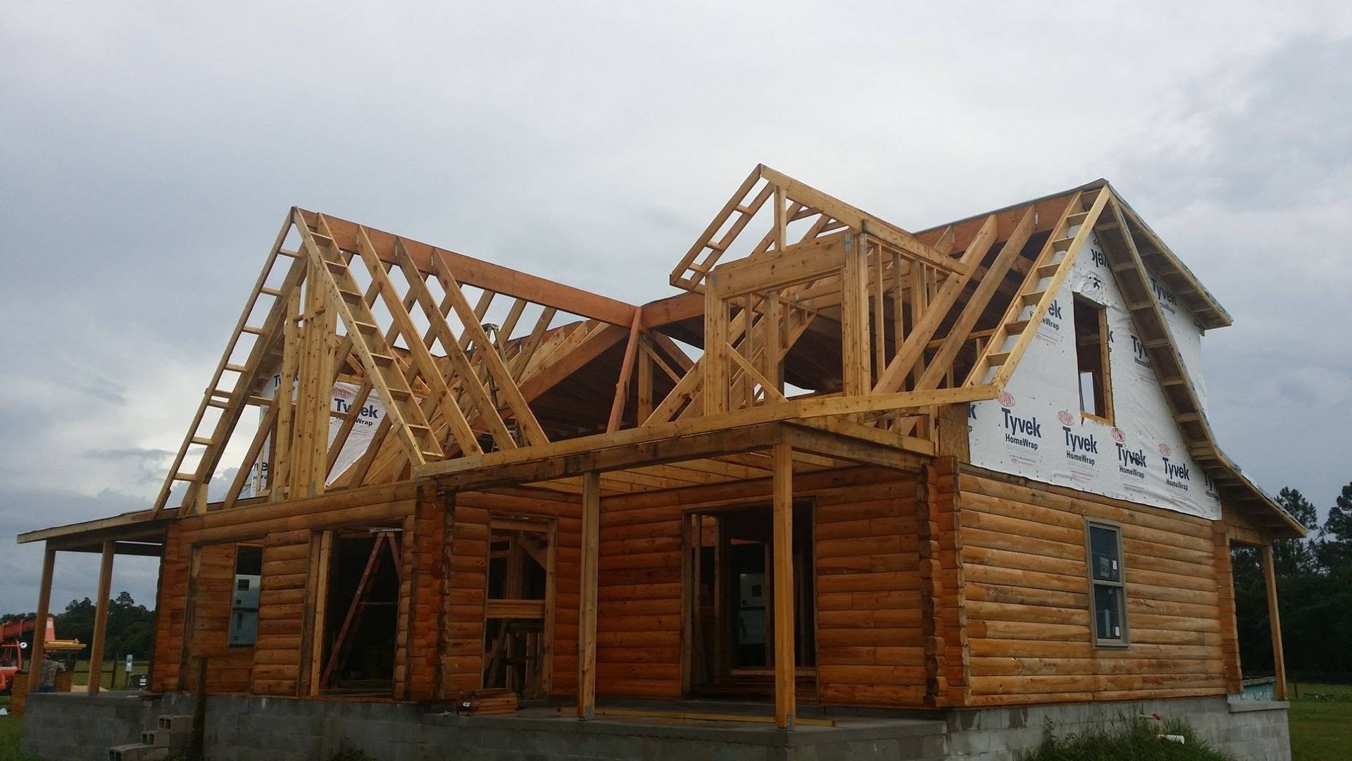 Partially built timber-frame house with exposed roof trusses under cloudy sky