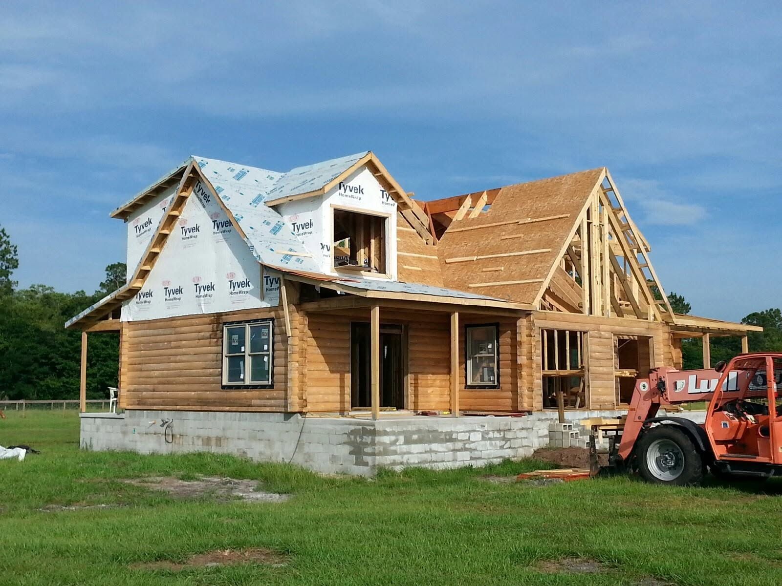 Partially built house with exposed framing and white siding, with a red tractor beside it