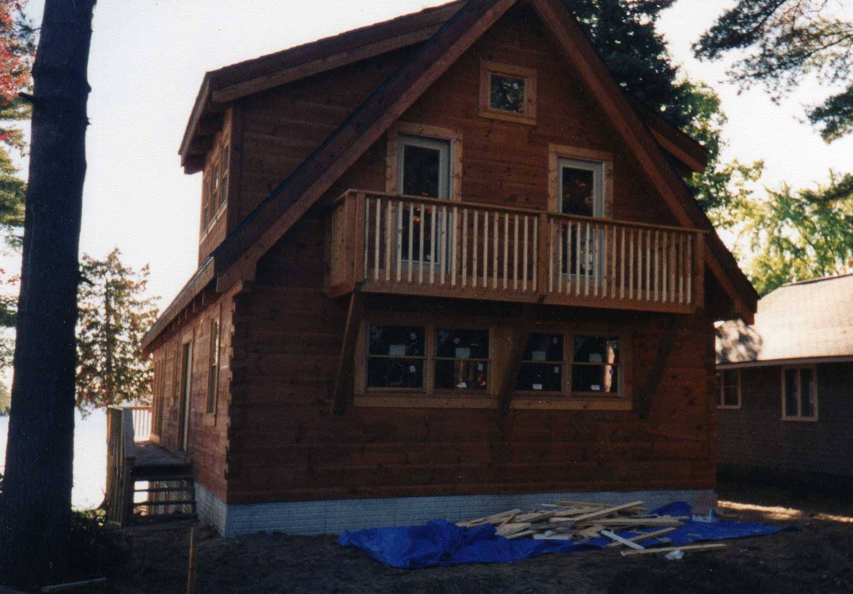 Wooden cabin with a small balcony and blue tarp on the ground, viewed from the front.