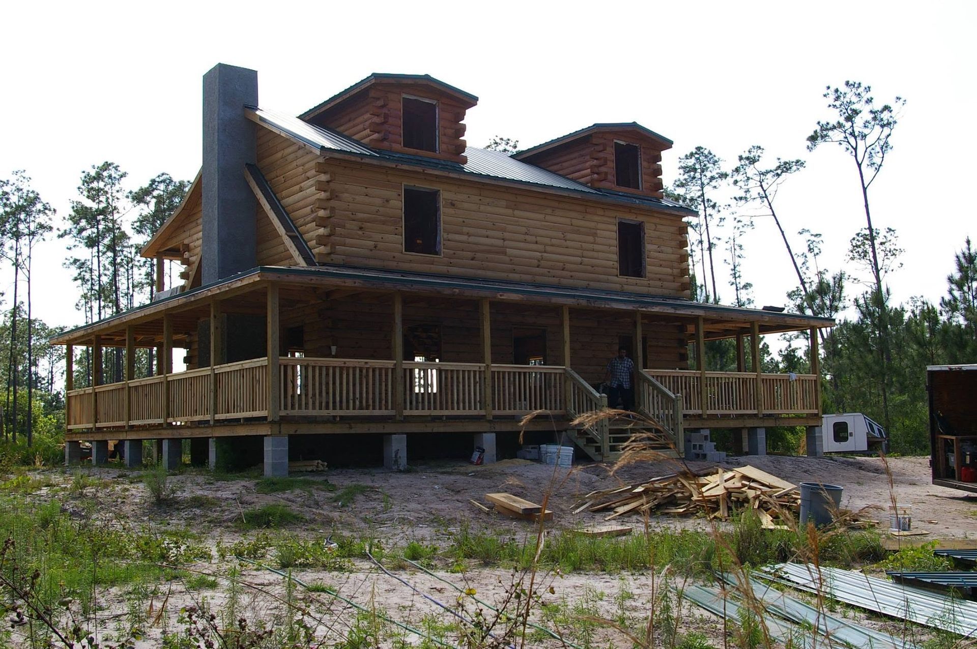 Partly built wooden log cabin with wraparound porch in a wooded clearing